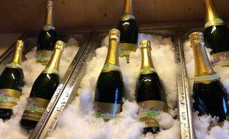 Sechs Flaschen Sekt liegen in einer Eiswanne. Die Flaschen sind mit goldenen Kappen und Etiketten versehen.