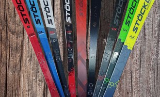 A selection of skis from the brand Stöckli in various colors and designs. The skis are placed on a wooden surface. | © Austrian Ski- & Service Ranch | Trixi Leitner