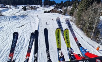 Eine Skiliftfahrt über eine verschneite Piste. Im Vordergrund sind mehrere Skier zu sehen, im Hintergrund führt die Piste durch eine Winterlandschaft. | © Austrian Ski- & Service Ranch | Trixi Leitner