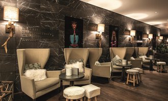 Ein modernes Café mit gemütlichen Sitzecken und stilvollem Dekor. Die Wände sind mit kunstvollen Bildern dekoriert und es gibt sanfte Beleuchtung. | © Travel Charme Ifen Hotel