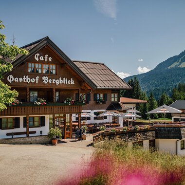 Ein gemütlicher Gasthof mit einem schönen Café und Blick auf die Berge. Umgeben von grünen Wiesen und einem klaren blauen Himmel.