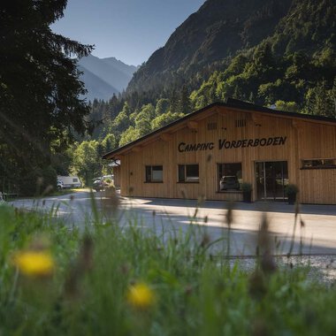 Ein Holzgebäude mit dem Schriftzug "Camping Vorberdoden" in einer grünen Umgebung. Im Hintergrund sind Berge und Bäume zu sehen. | © Campingplatz Vorderboden GmbH | Marion Schwendiger