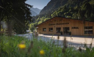 A wooden building with the inscription "Camping Vorberdoden" in a green environment. In the background, mountains and trees can be seen. | © Campingplatz Vorderboden GmbH | Marion Schwendiger