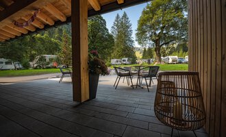 A cozy terrace with a table and chairs, surrounded by trees and meadows. In the background, there are motorhomes at a campsite. | © Campingplatz Vorderboden GmbH | Marion Schwendiger