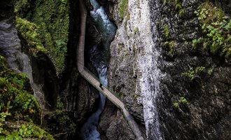 Eine malerische Schlucht mit steilen Felsen und einem fließenden Bach. Üppiges Grün umgibt die Umgebung und schafft eine ruhige Atmosphäre. | © Breitachklamm | Dominik Berchtold