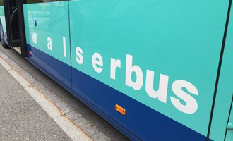 Ein Bus mit der Beschriftung „walserbus“ in blauer und grüner Farbe. Der Bus steht entlang einer Straße. | © Kleinwalsertal Tourismus