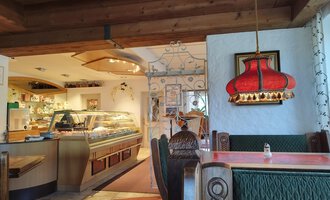 A cozy restaurant with wooden furniture and a warm atmosphere. In the background, there is a bar and a striking red lamp visible. | © Kleinwalsertal Tourismus | N. Lughammer