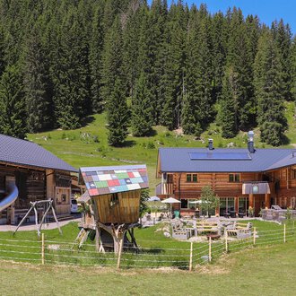 © Naturzeithof Café für dich | Stefanie Conticello Ein malerisches Bergdorf mit traditionellen Holzhäusern und einer grünen Wiese. Umgeben von hohen Bäumen und klarem Himmel. | © Naturzeithof Café für dich | Stefanie Conticello
