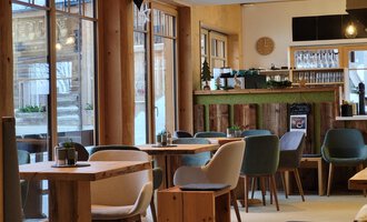 Ein modernes Café mit Holzmöbeln und großen Fenstern. Die farbenfrohen Stühle und die gemütliche Atmosphäre laden zum Verweilen ein.