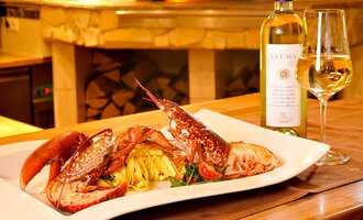 Ein leckerer Teller mit frischem Hummer und Pasta, begleitet von einem Glas Weißwein. Im Hintergrund ist eine gemütliche Restaurantatmosphäre zu sehen. | © Ristorante Trentino | Michael Monschau