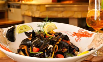 Ein schmackhaftes Gericht mit Muscheln, Gemüse und Zitronenscheiben. Im Hintergrund steht ein Glas mit einem erfrischenden Getränk. | © Ristorante Trentino | Michael Monschau