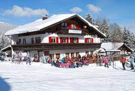 A traditional chalet in the snow with red shutters. Many people enjoy winter activities around the building.