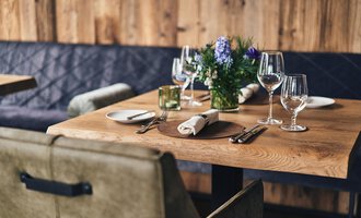 Ein schön gedeckter Tisch in einem gemütlichen Restaurant. Die Holzoberfläche ist mit Gläsern, Geschirr und einer Blume dekoriert. | © A-ROSA Ifen Hotel Kleinwalsertal