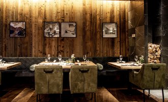 Ein modernes Restaurant mit Holzwänden und stilvollen Möbeln. Die Tische sind elegant gedeckt und an der Wand hängen Bilder. | © A-ROSA Ifen Hotel Kleinwalsertal