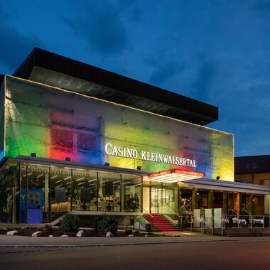 Ein modernes Casino mit bunten Lichtern in der Abenddämmerung. Es befindet sich im Kleinwalsertal und hat eine stilvolle Architektur. | © Casinos Austria | Arnd Ötting