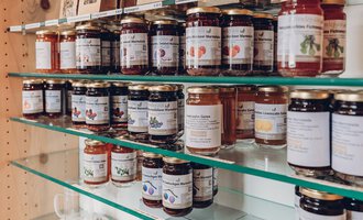 Eine Sammlung von Marmeladengläsern auf einem Regal. Die Gläser sind in verschiedenen Farben und mit Etiketten beschriftet. | © Carolin Ries | www.calejofotografie.de