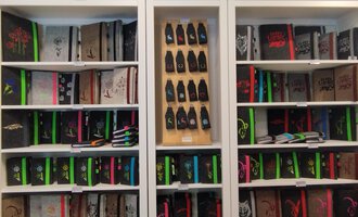 Eine Regalwand mit vielen Notizbüchern in verschiedenen Farben und Designs. Darunter befinden sich farbige Stifte und weitere Schreibwaren. | © Chrömle Schönes aus Filz | N. Lughammer