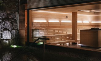 A modern sauna with bright wood interiors and soft lighting. In the background, stones and a relaxing atmosphere can be seen. | © Naturhotel Chesa Valisa