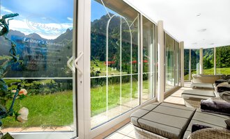 A modern room with large windows that offer a view of a green landscape and mountains. Cozy loungers invite you to relax. | © Hotel Leitner