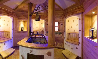 Ein gemütlicher Wellnessbereich mit Holzverkleidung und sanfter Beleuchtung. In der Mitte steht ein runder Brunnen, umgeben von Sitzgelegenheiten. | © Hotel Leitner