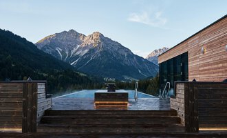 Ein Infinity-Pool mit Blick auf majestätische Berge. Die Holzveranda schafft eine gemütliche Atmosphäre in der Natur. | © A-ROSA Ifen Hotel Kleinwalsertal