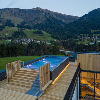 © Genuss- & Aktivhotel Sonnenburg |Heike Wohlgenannt Eine moderne Terrasse mit einem Pool und Holzfußboden, umgeben von malerischen Bergen. Die Aussicht auf die Landschaft ist atemberaubend und vermittelt ein Gefühl von Ruhe. | © Genuss- & Aktivhotel Sonnenburg |Heike Wohlgenannt
