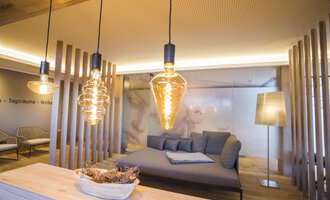 Ein modernes Wohnzimmer mit stilvollen Lichtquellen und gemütlichem Sofa. Die Wände sind hell und der Raum hat eine entspannte Atmosphäre. | © Genuss- & Aktivhotel Sonnenburg | Frank Drechsel