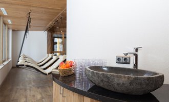 A modern bathroom with an elegant stone table and a sink. In the background, cozy loungers and large windows can be seen. | © Hotel Alpenstüble Appartements | Manuel Riezler