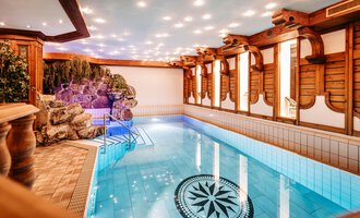 Ein schöner Innenpool mit klarem, blauem Wasser und dekorativen Holzelementen. Die Atmosphäre ist ruhig und einladend, perfekt zum Entspannen. | © Hotel Alpenstüble KG