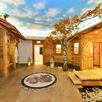 Ein gemütlicher Wellnessbereich mit Holzverkleidungen und einer schönen Baumdekoration. Die Decke zeigt einen klaren Himmel, der eine entspannende Atmosphäre schafft. | © Hotel Alpenstüble KG | Manuel Riezler