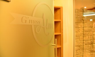 Eine Tür mit dem Schriftzug „G'nuss Alm“ ist im Bild sichtbar. Der Bereich scheint einladend und modern gestaltet zu sein. | © Hotel Alpenstüble KG | Manuel Riezler