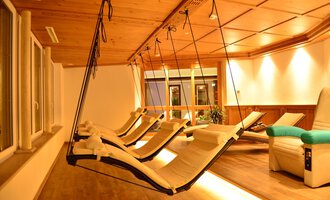 Ein gemütlicher Ruheraum mit hängenden Liegen und warmem Licht. Die Holzdecke schafft eine entspannende Atmosphäre. | © Hotel Alpenstüble KG | Manuel Riezler