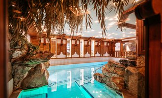Ein elegantes Hallenbad mit klarem Wasser und Felsen im Hintergrund. Die Holzverkleidung und die weiche Beleuchtung schaffen eine entspannte Atmosphäre. | © Hotel Alpenstüble KG