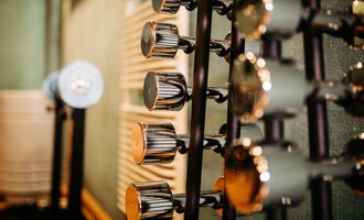 A series of dumbbells in a gym. The background is blurred and shows textures of the walls. | © Hotel Alpenstüble KG