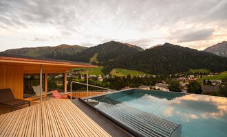 Ein schöner Ausblick auf die Berge von einer Terrasse mit einem Infinity-Pool. Die Wolken am Himmel verleihen der Szene eine entspannte Atmosphäre.