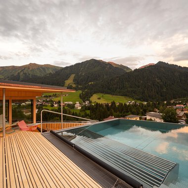 Ein schöner Ausblick auf die Berge von einer Terrasse mit einem Infinity-Pool. Die Wolken am Himmel verleihen der Szene eine entspannte Atmosphäre.