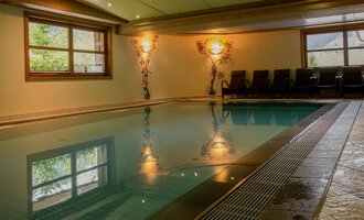 Ein schöner Innenpool mit beleuchteten Wänden und entspannenden Liegen. Das Wasser reflektiert die Umgebung und schafft eine ruhige Atmosphäre. | © IFA Hotel Alpenhof Wildental | Andreas Froschauer