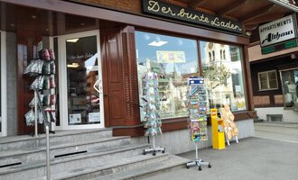 A store called "The Colorful Shop" with large windows and an inviting entrance. Outside are several stands with postcards and souvenirs. | © Der Bunte Laden | Romana Volderauer