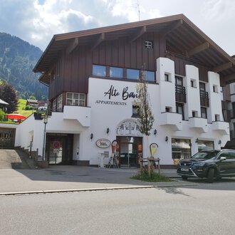 © Kleinwalsertal Tourismus | N. Lughammer A modern building with a wooden and plaster facade that offers apartments. In the background, green mountains and a blue sky can be seen. | © Kleinwalsertal Tourismus | N. Lughammer