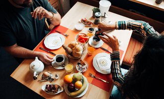 A laid table with breakfast, including rolls, fruit, and coffee. Two people enjoy the food and the cozy atmosphere.