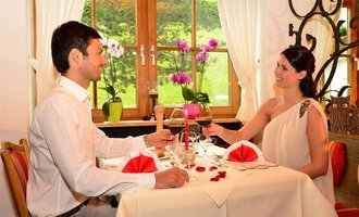 A romantic dinner for two people in a cozy restaurant. The table is decorated with red napkins and flowers, and the guests enjoy glasses of wine. | © Sport und Familienhotel Riezlern