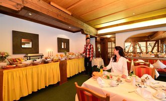 A cozy breakfast room with a rich buffet and freshly set tables. Two people are enjoying the inviting atmosphere. | © Sport und Familienhotel Riezlern