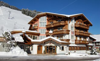 A beautiful chalet in the snow with many balconies and wooden decorations. In the background, snow-covered mountains can be seen. | © Hotel Alpenstüble Appartements | Manuel Riezler