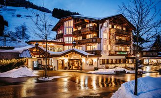 Ein charmantes Hotel im Winter mit schneebedeckten Bergen im Hintergrund. Die warmen Lichter des Hauses strahlen in der Abenddämmerung. | © Hotel Alpenstüble KG