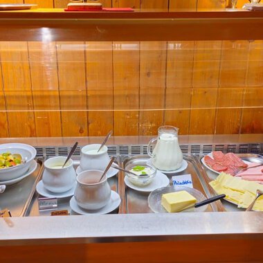 Ein reichhaltiges Frühstücksbuffet mit verschiedenen Käsesorten, Aufschnitt, Joghurt, Müsli und frischem Obst. Dazu gibt es Milch und Säfte. | © Hotel Garni Adler | Mennel&Feurstein Immo Invest GmbH