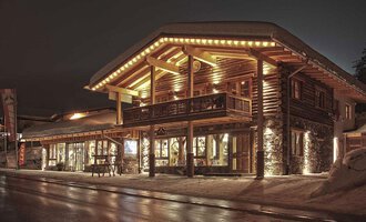 Ein gemütliches Holzgebäude mit warmem Licht in der Nacht. Der schneebedeckte Boden und das stilvolle Design schaffen eine einladende Atmosphäre. | © Fun-Alp