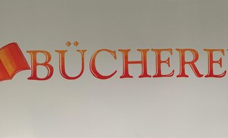 Eine kreative Wandgestaltung mit dem Wort "Bücherei". Neben dem Text ist ein riesiges, offenes Buch abgebildet. | © Kleinwalsertal Tourismus | N. Lughammer