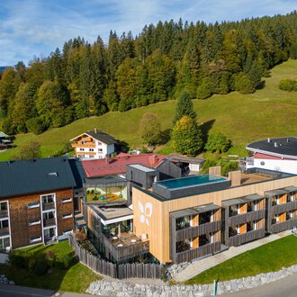 Ein modernes Hotelgebäude in einer malerischen Landschaft mit grünen Wiesen und bewaldeten Hügeln. Die Umgebung ist ruhig und einladend, ideal für Erholungssuchende.