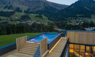 Ein modernes Gebäude mit einem Außenpool auf einer Terrasse. Im Hintergrund sind die Berge und die Natur zu sehen.