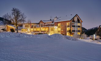 Ein schönes Chalet im Schnee mit beleuchteten Fenstern. Der Himmel ist klar und es ist Abenddämmerung.